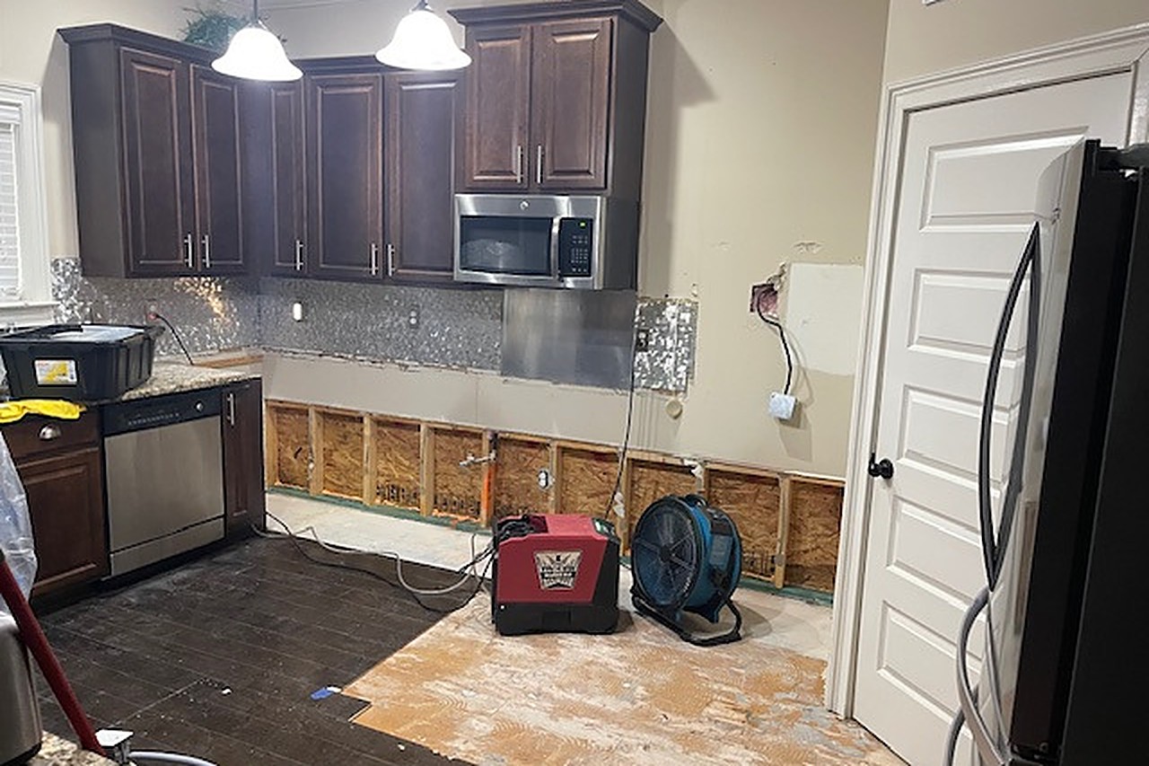 Air movers and dehumidifier drying the kitchen after flood cuts at the cabinet bases